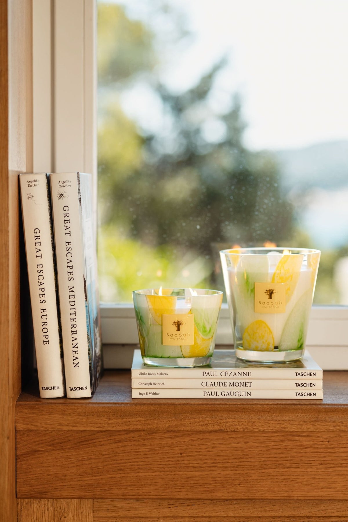 Shop Baobab Collection Santo Sospir scented candles styled on top of art books next to a bright window with Mediterranean decor elements.