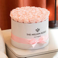 A round white gift box filled with pale pink roses, wrapped with a pink ribbon and bow. The front of the box reads 'THE MILLION ROSES Los Angeles.